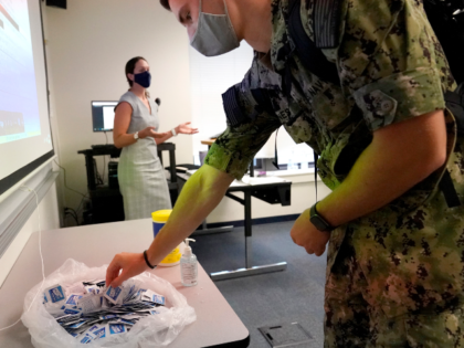 A midshipman reaches for sanitizing wipes while arriving to a leadership class taught by p