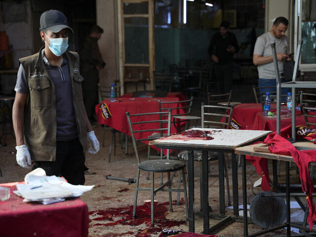 A forensic investigator wearing gloves walks through the damaged interior of a cafe in cen