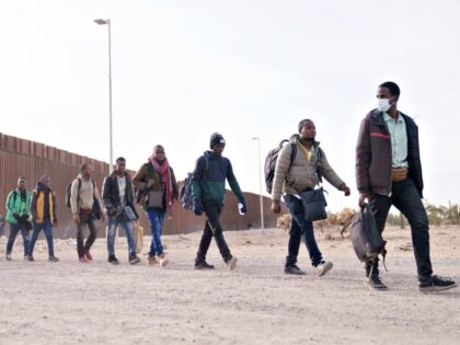 Migrants walk beside the US-Mexico border fence in Lukeville, Arizona, US, on Monday, Dec.