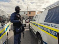 A South African policeman secure the perimeter while a house is searched for guns, drugs and counterfeit goods during the crime prevention operation Shanela in Tafelsig, Cape Town on February 13, 2026. Operation Shanela, "to sweep" in Setswana, is a high-density, multi-disciplinary, and countrywide crime-fighting initiative led by the South African Police Service (SAPS) to combat serious crime, specifically targeting hotspots, illegal mining, and unlicensed firearms. (Photo by GIANLUIGI GUERCIA / AFP via Getty Images)