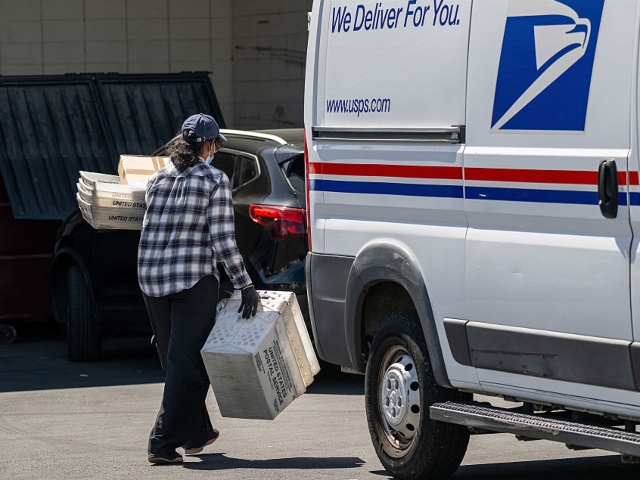 GettyImages-2267824229 A United States Postal Service (USPS) worker carries containers and packages from a vehicl