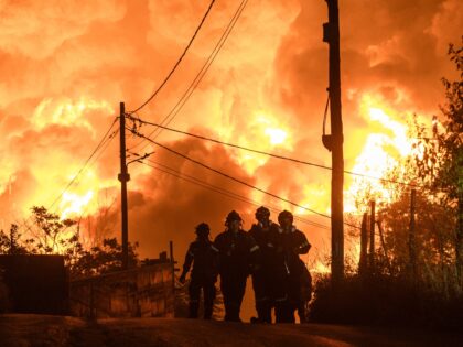 Firefighters walk away from a burning factory during a wild fire near Oraiokastro, on the