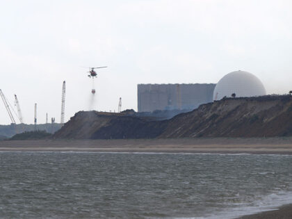 A helicopter flies water collected from the sea to drop on the wildfire at Dunwich Heath,