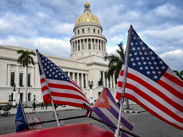 Two US flags and a Cuban flag flutter on the roof of a tricycle in front of the Capitolio