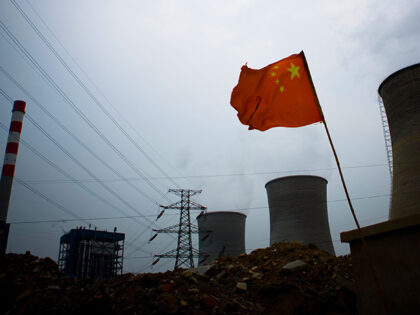 A Chinese flag flies in front of a coal fired power plant rising across the skyline of rap