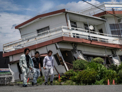 Workers walk past a damaged house and partially collapsed in Yatsushiro, Kumamoto prefectu