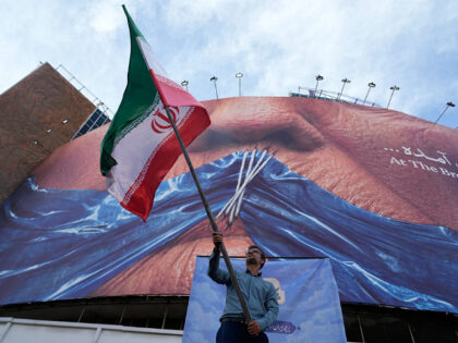 A man waves an Iranian flag for a pro-government campaign under a billboard with graphic s