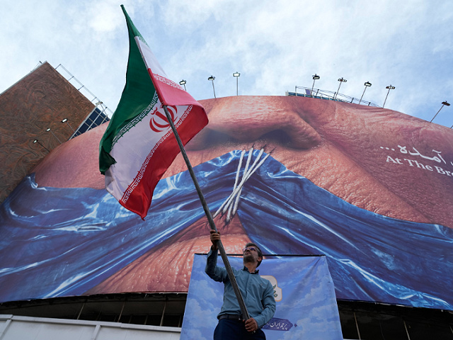 A man waves an Iranian flag for a pro-government campaign under a billboard with graphic showing Strait of Hormuz and sewn lips of U.S. President Donald Trump in a square in downtown Tehran, Iran, Wednesday, May 6, 2026. (AP Photo/Vahid Salemi)