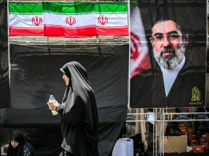 A woman walks past images of Iran's current supreme leader Mojtaba Khamenei (R) and his pr