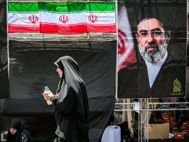 A woman walks past images of Iran's current supreme leader Mojtaba Khamenei (R) and his pr
