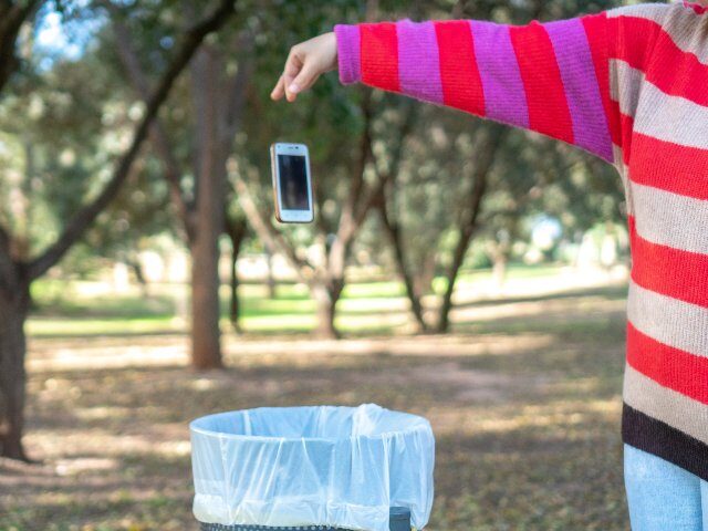 close-up of a hand throwing a mobile phone in the trash