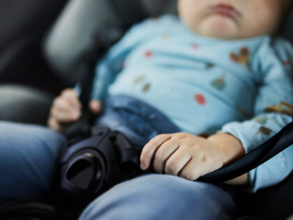 Infant sleeping in a rear-facing car seat with hand on buckle, highlighting child safety,