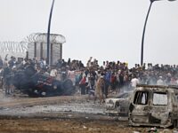 People gather next to an overturned and burnt vehicles at the site of clashes near Fnideq, on the Morocco-Spain border, on July 31, 2026. Thousands of migrants crossed overnight from Morocco into Spain's north Africa's Ceuta enclave, a police source said on July 31, adding that it was impossible to estimate how many people in total. A total of 18 people died while attempting to reach the Spanish enclave, the source said. (Photo by Abdel Majid BZIOUAT / AFP)