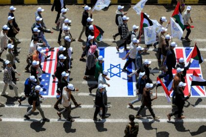 University students walk on the US, Israeli, and UK flags at a protest in Yemen's San