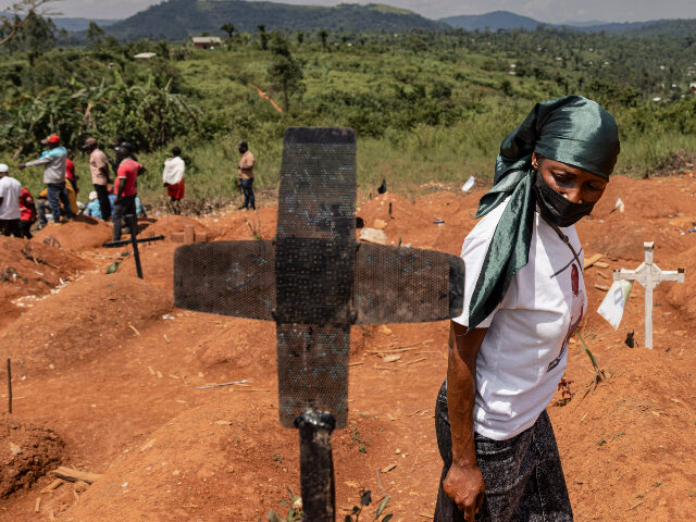 Ebola DRC MAY 20: A woman wearing a mask walks by a grave marker for an Ebola victim as people atten