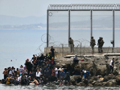 TOPSHOT - Migrants stand on rocks as Spanish soldiers stand guard at the border fence of t