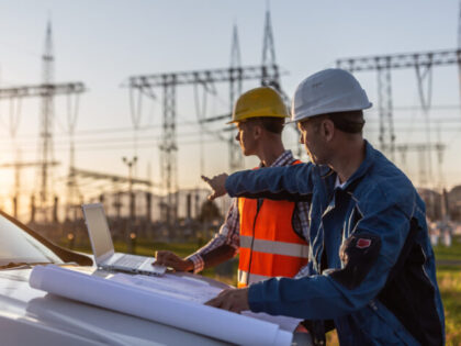 Blue collar worker points towards sun setting over power distribution center with white co
