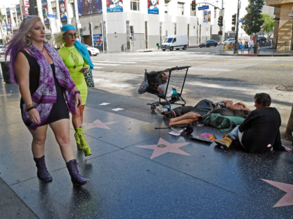 Los Angeles, CA - August 12: People who are displaced sit on the sidewalk with two dogs on