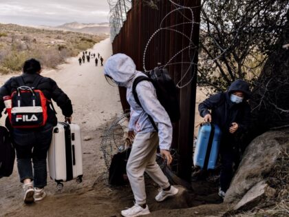 Migrants cross through a gap in the US-Mexico border fence in Jacumba Hot Springs, Califor