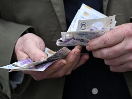 A bookmaker handles a wad of pound notes as racegoers place bets at a betting stand ahead