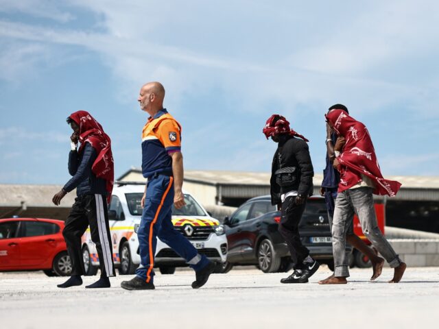 Migrants walk with a member of France's Civil Defence after disembarking from a French res