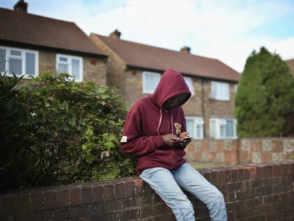 LONGFORD, ENGLAND - OCTOBER 14: A young asylum seeker checks his phone while sitting on a