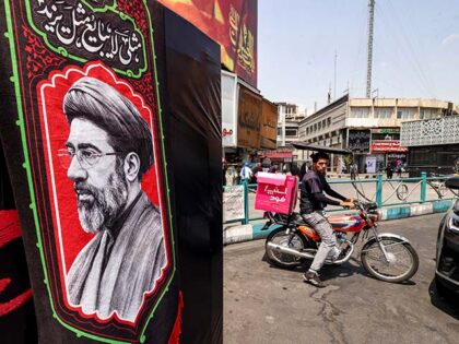 A delivery person rides a motorcycle near an image of Iran's Supreme Leader Mojtaba Khamen
