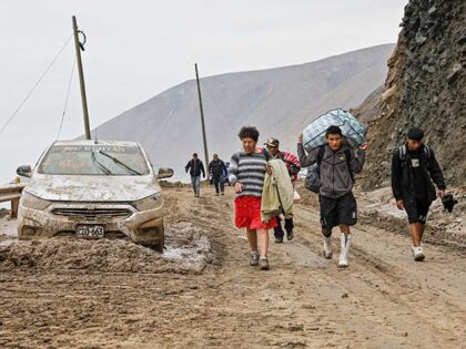People walk past a car trapped in a mudslide on the Pan-American Highway between the secto