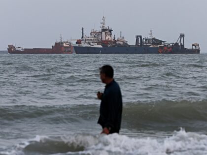 BANDAR ABBAS, IRAN - AUGUST 10: A person wades in the water as ships are seen anchored in