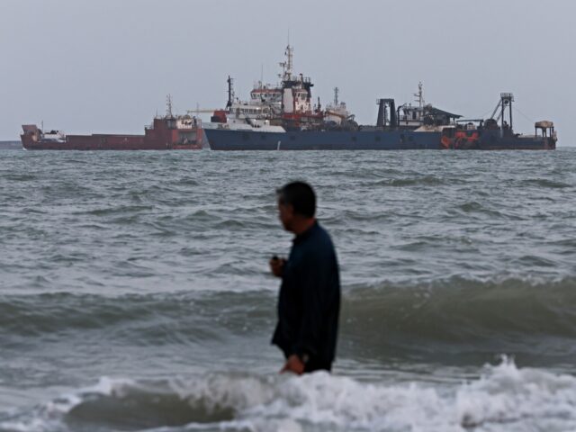 BANDAR ABBAS, IRAN - AUGUST 10: A person wades in the water as ships are seen anchored in