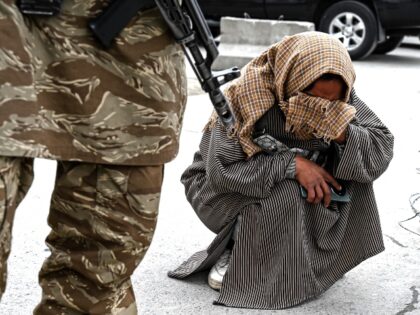 A Taliban security officer stands guard as Afghan woman Samira Muhammadi weeps while searc