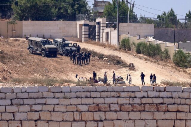 Israeli soldiers stand guard next to settlers in front of Palestinian houses in the villag