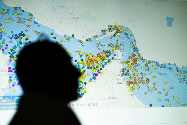 A person in front of a large screen displaying vessel movements in the Strait of Hormuz on