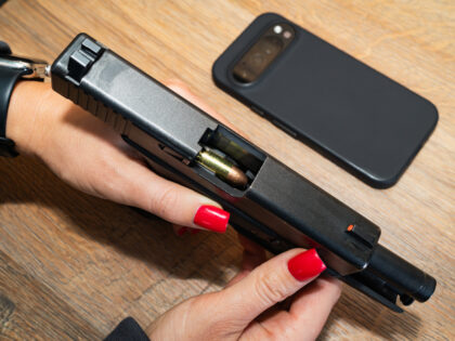 The girl is holding a 9mm pistol and there is a mobile phone lying nearby.