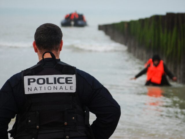 A French policeman looks at a migrant wading to the shore after attempting to cross the En