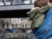 A pedestrian holds a child as he walks past tents at a temporary migrant camp under an elevated section of Metro line 2, in the La Chapelle district of Paris on May 7, 2026. (Photo by Joel Saget / AFP via Getty Images)