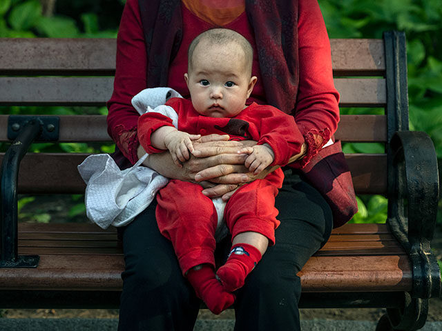 GettyImages1232843439 A woman holds a baby at a local park on May 12, 2021 in Beijing, China. According to data