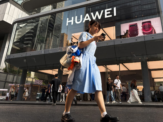 Huawei A pedestrian looks at a smartphone while walking past a Huawei retail store displaying an