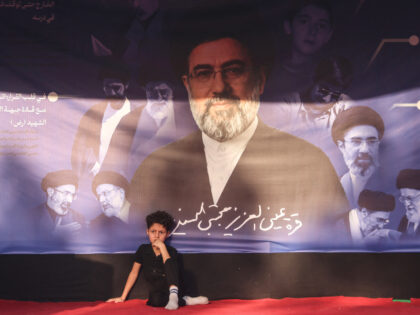 A boy sits beneath a banner depicting Iranian supreme leader Mojtaba Khamenei as Shia pilg