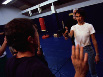 Woman points gun at man in self-defense class at a fantasy spy camp. (Photo by © Erik Fre