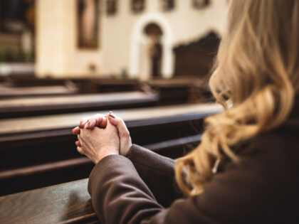 Christian woman with hands folded in prayer sitting on church pew. Religion and spirituali