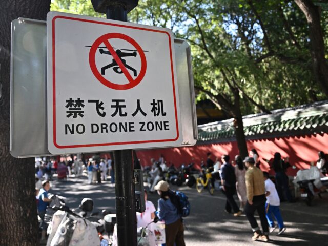 People walk past a sign reading "No drone zone" in an alley in Beijing on September 14, 20