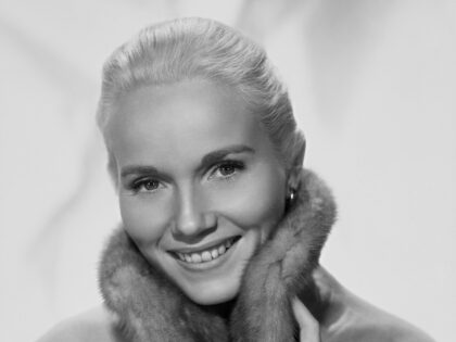 American actress Eva Marie Saint smiling as she holds the fur-trimmed collar of her coat c