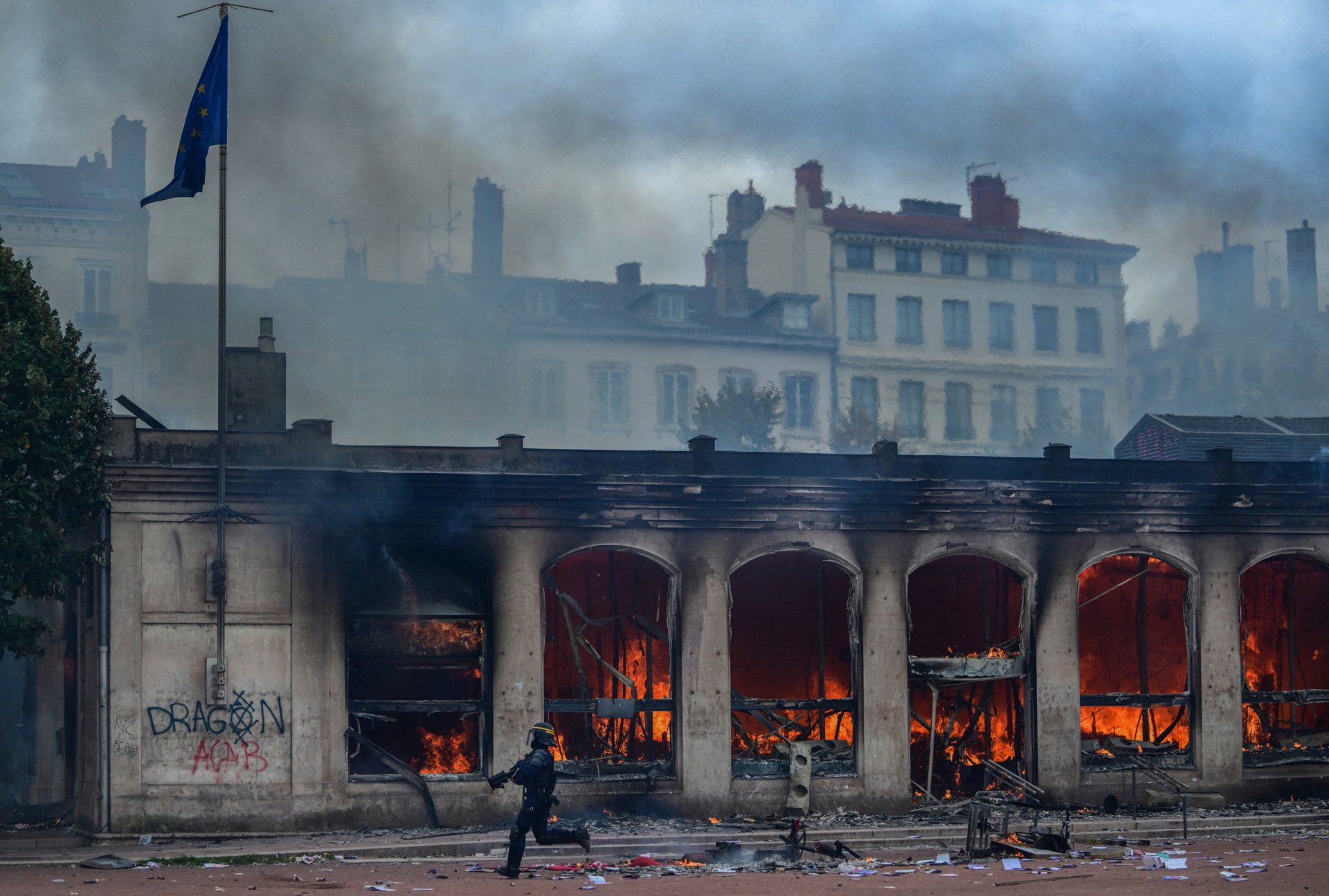 A member of French Republican Security Corps (CRS - Compagnies Republicaines de Securite) runs in front of Lyon's tourism office set on fire during a demonstration to protest against the "high cost of living", in Lyon, southeastern France, on October 17, 2026 as part of a nationwide call for mobilisation bringing together various groups expressing their anger: former "Yellow Vest", secondary school and university students, climate activists and even farmers. After weeks of student protests, France faces broader, nationwide demonstrations on October 17, 2026 over the cost of living, setting up a potentially fraught six months heading into a presidential election. A police source told AFP that authorities estimated nearly 200,000 people could take part, with 40,000 in Paris. (Photo by OLIVIER CHASSIGNOLE / AFP via Getty Images)
