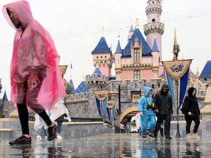 Disneyland guests walk past the Sleeping Beauty Castle while visiting Disneyland amid rain