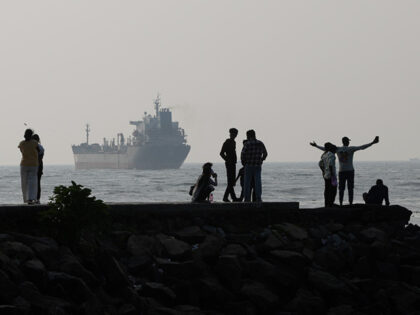 Domestic tourists stand on the seaside promenade at Fort Kochi beach as the oil and chemic